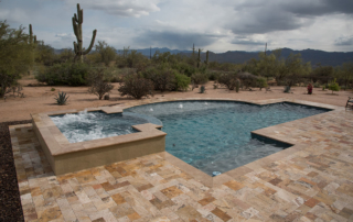 Pool and raised spa with travertine decking in a desert setting with saguaros
