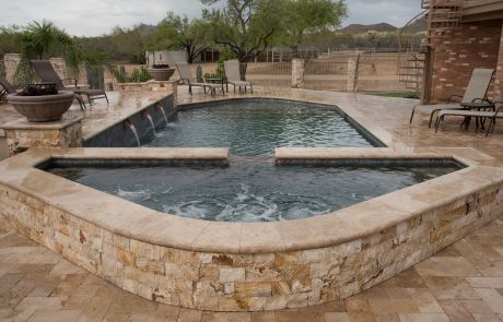 Raised spa with a travertine stone face spilling into the pool