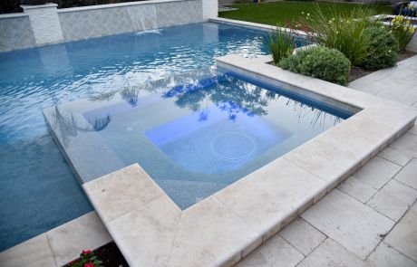 Pool with an attached travertine-edged spa and planters