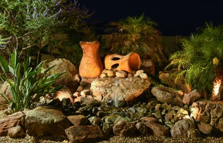 Lit rock water feature with clay pots and desert plants at night