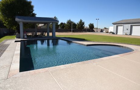 Freeform pool with a ramada beyond and concrete decking