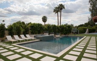 Rectangular pool with paver-and-turf grid decking, loungers and palm trees