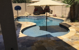 7after Remodeled freeform pool with a sun shelf umbrella and travertine decking