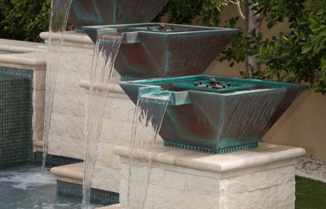 Three copper water bowls on stone pedestals spilling into the pool