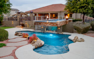 Freeform pool with boulders and a raised spa spilling over a waterfall, with fire bowls at dusk