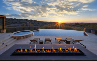 Overflow Pools PebbleSheen Vanishing-edge pool and spa with a linear fire feature at sunset over the desert