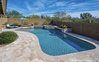 Freeform pool with a pebble finish and travertine decking in a desert setting